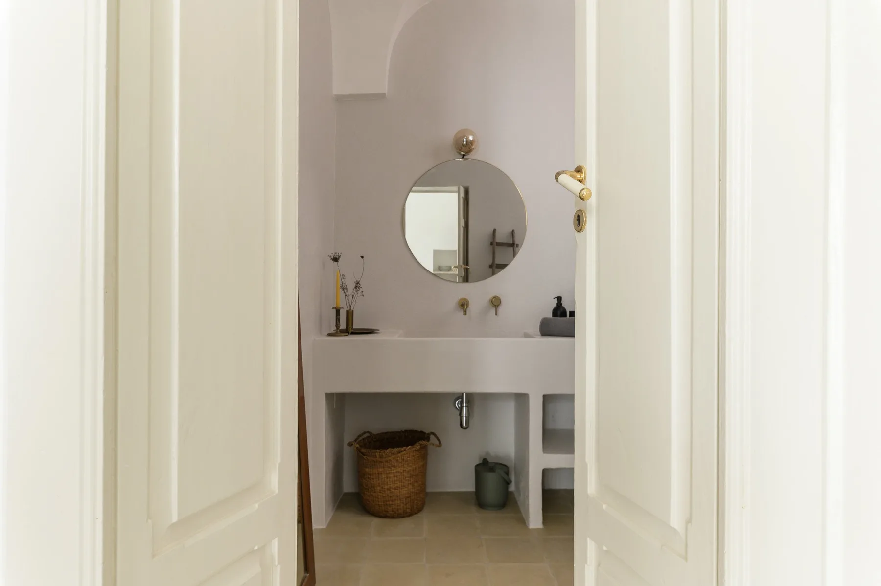 A bathroom vanity with a round mirror and storage shelves below.