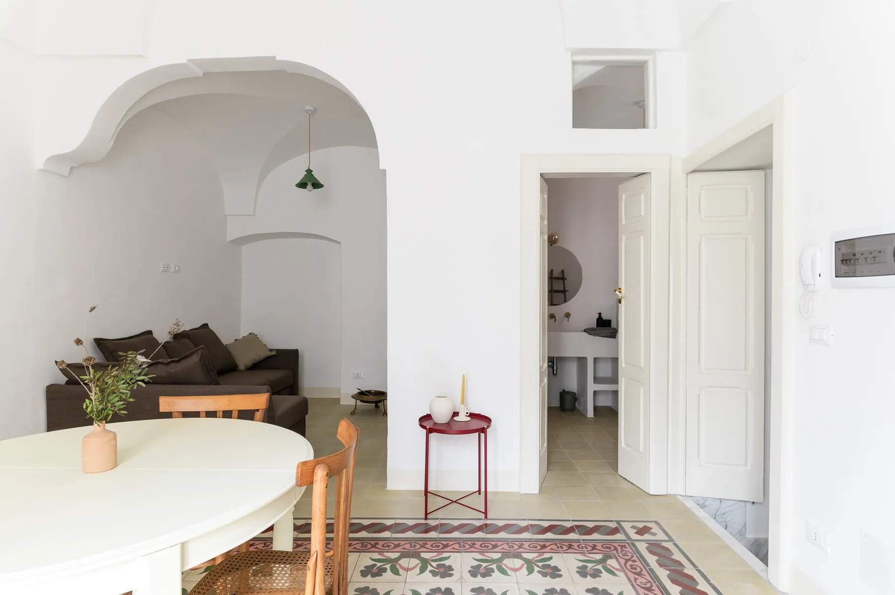 A bright dining and living area with a round table and seating beside an open doorway.