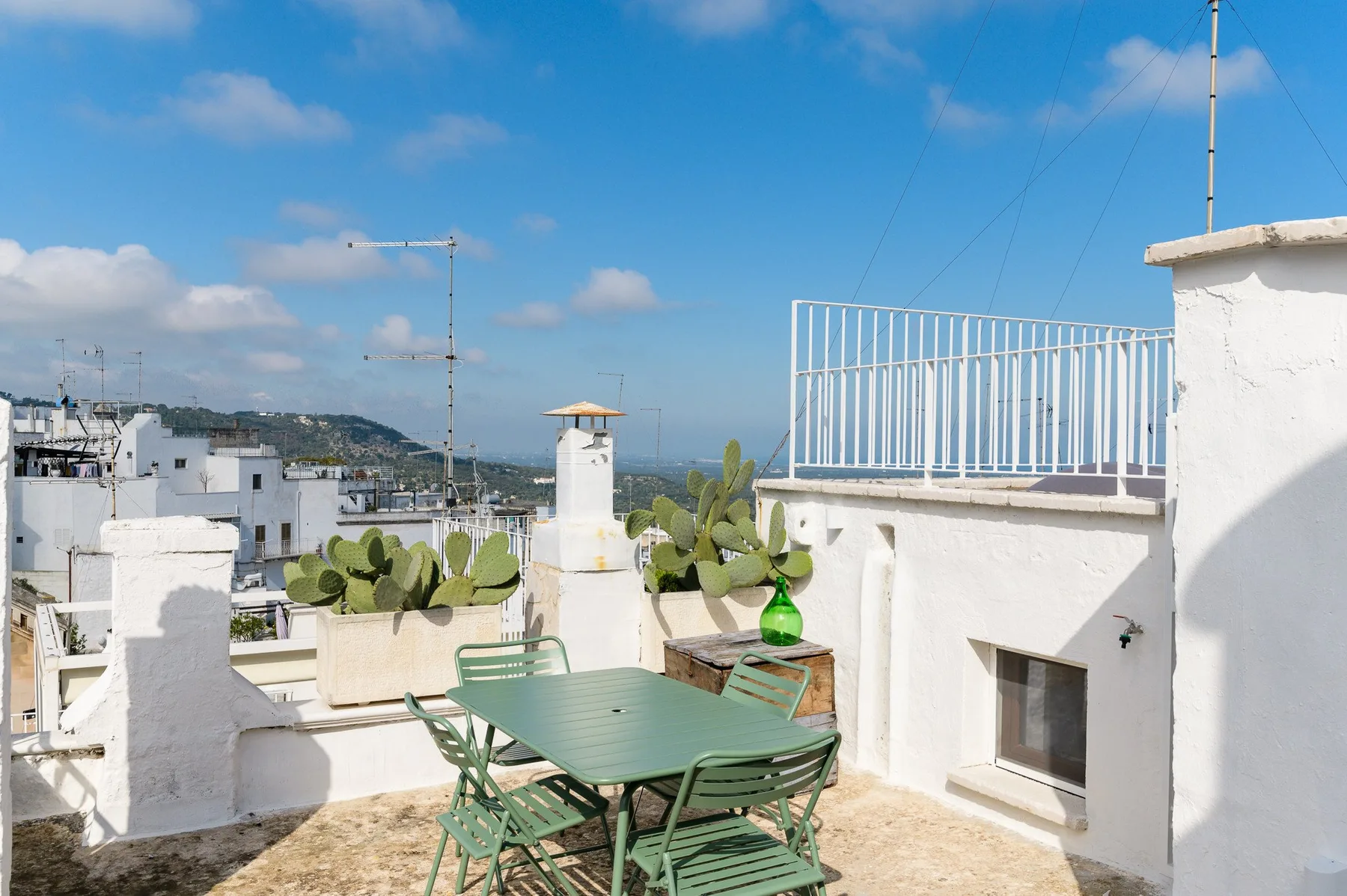 A rooftop terrace has green outdoor seating and views of nearby buildings.
