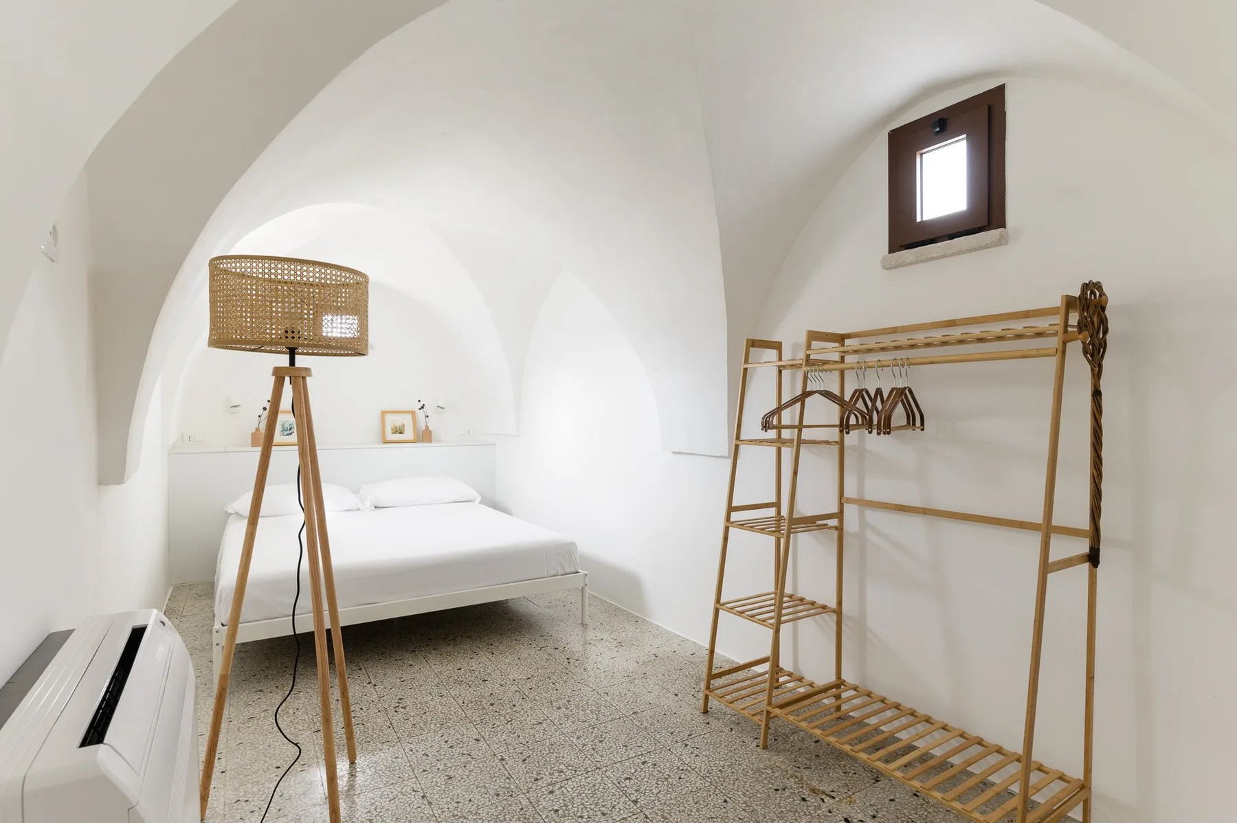 A bright bedroom with a bed, a floor lamp, and a clothing rack.