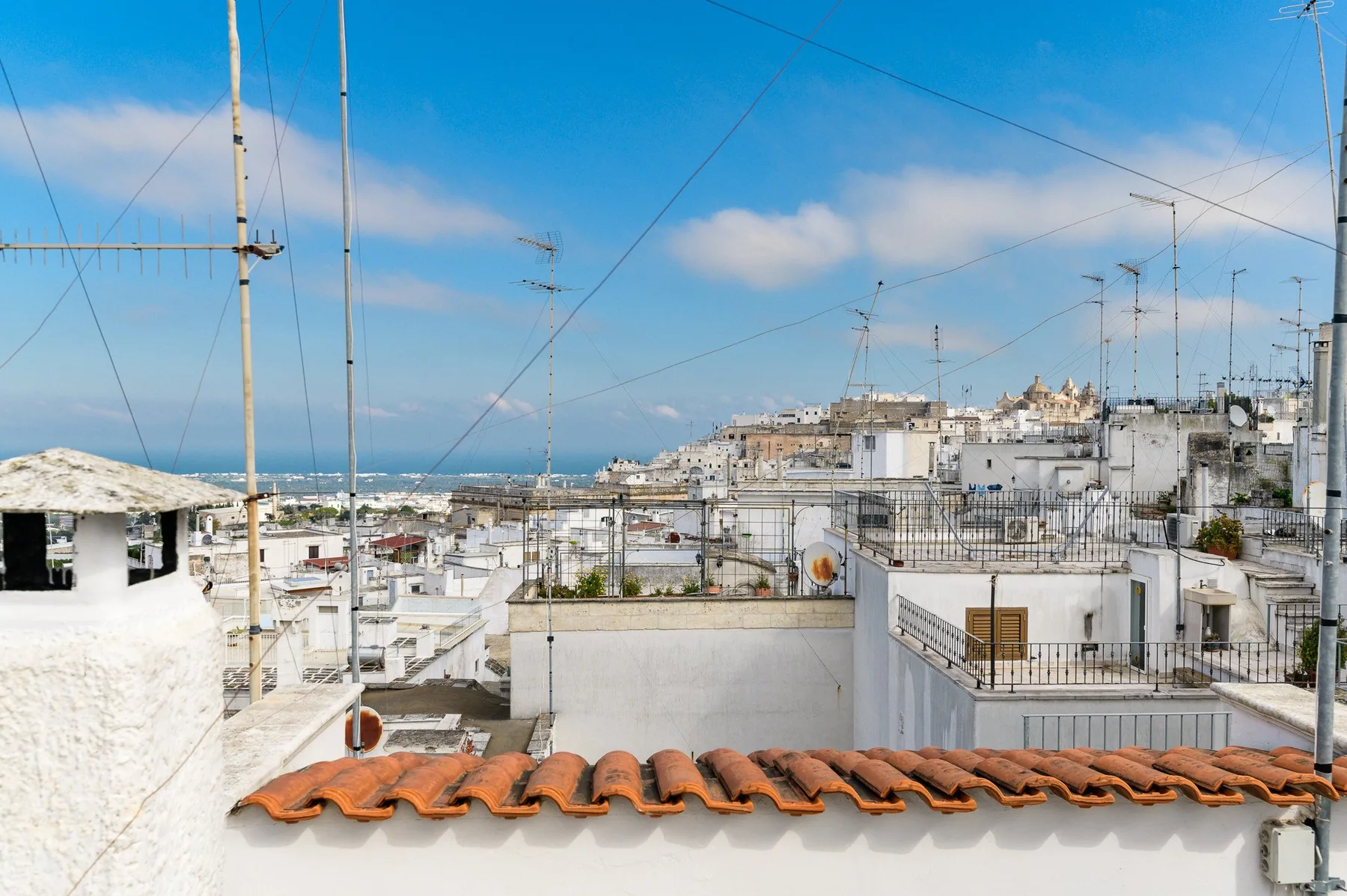Rooftop view across white buildings toward the sea under a blue sky.