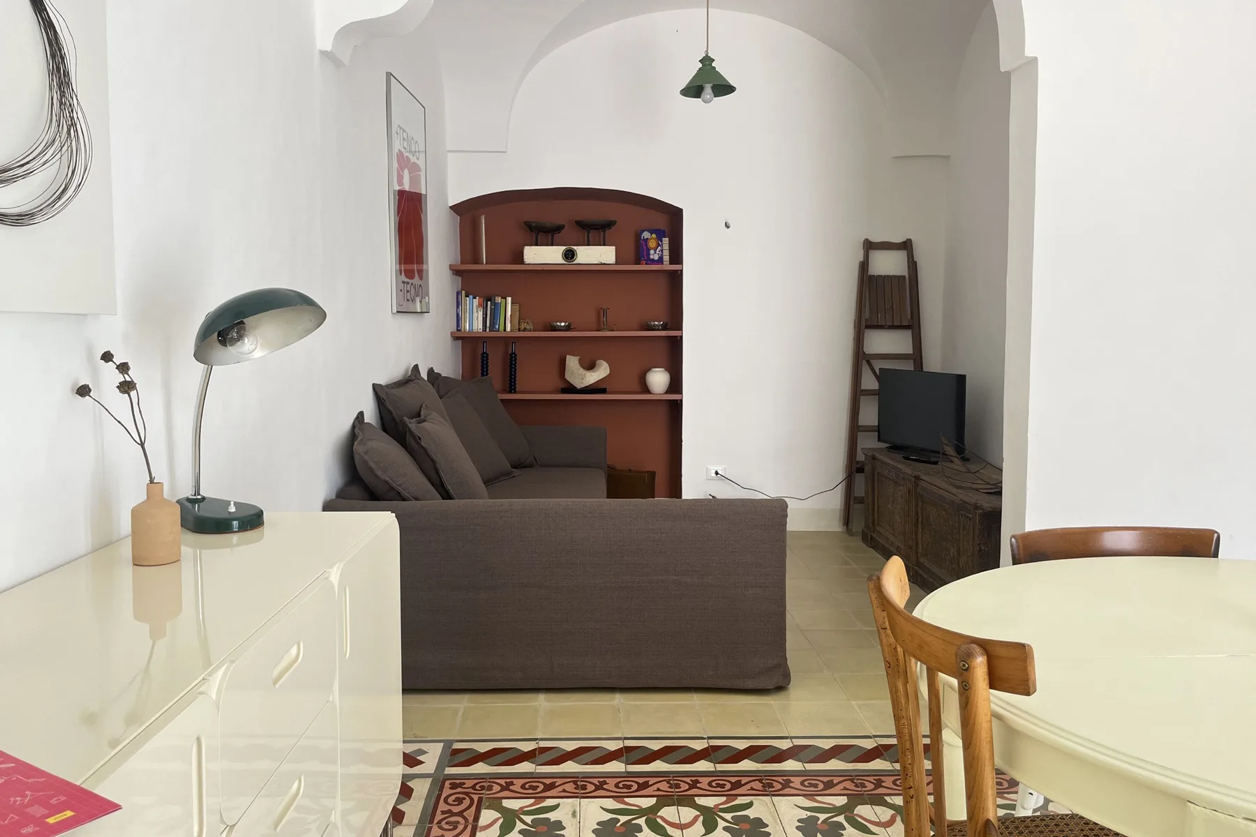 A living room with a brown sofa, wooden shelves, and a dining table.