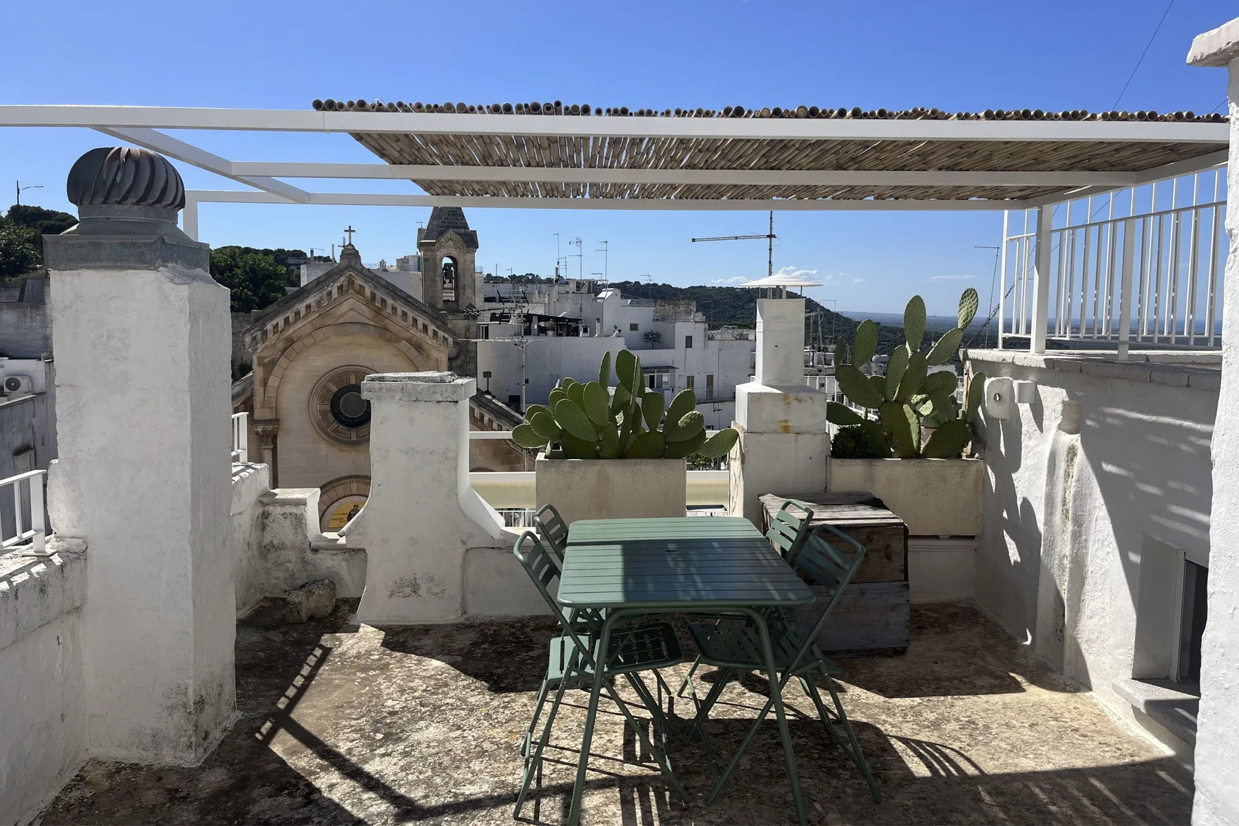 A rooftop terrace with an outdoor table and potted plants overlooks nearby buildings.