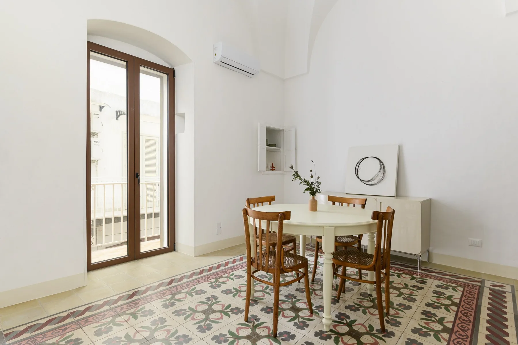 A dining area with a wooden table and chairs on a patterned tile floor.
