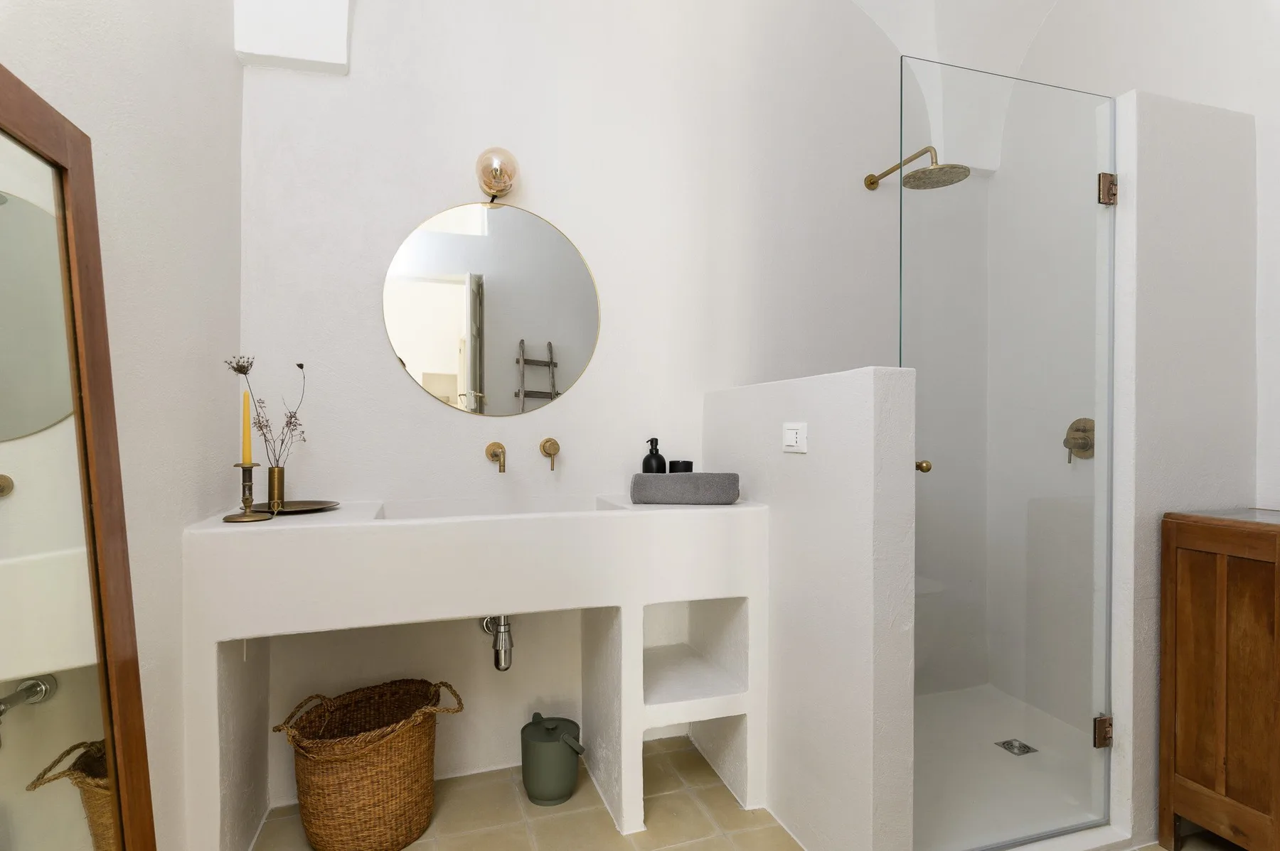 A bright bathroom with a white sink, round mirror, and glass shower.