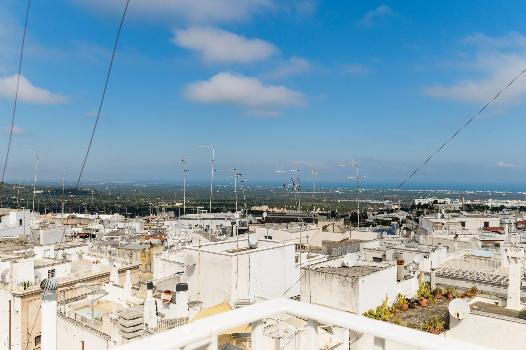 A rooftop terrace overlooks a dense cluster of white buildings and the distant sea.