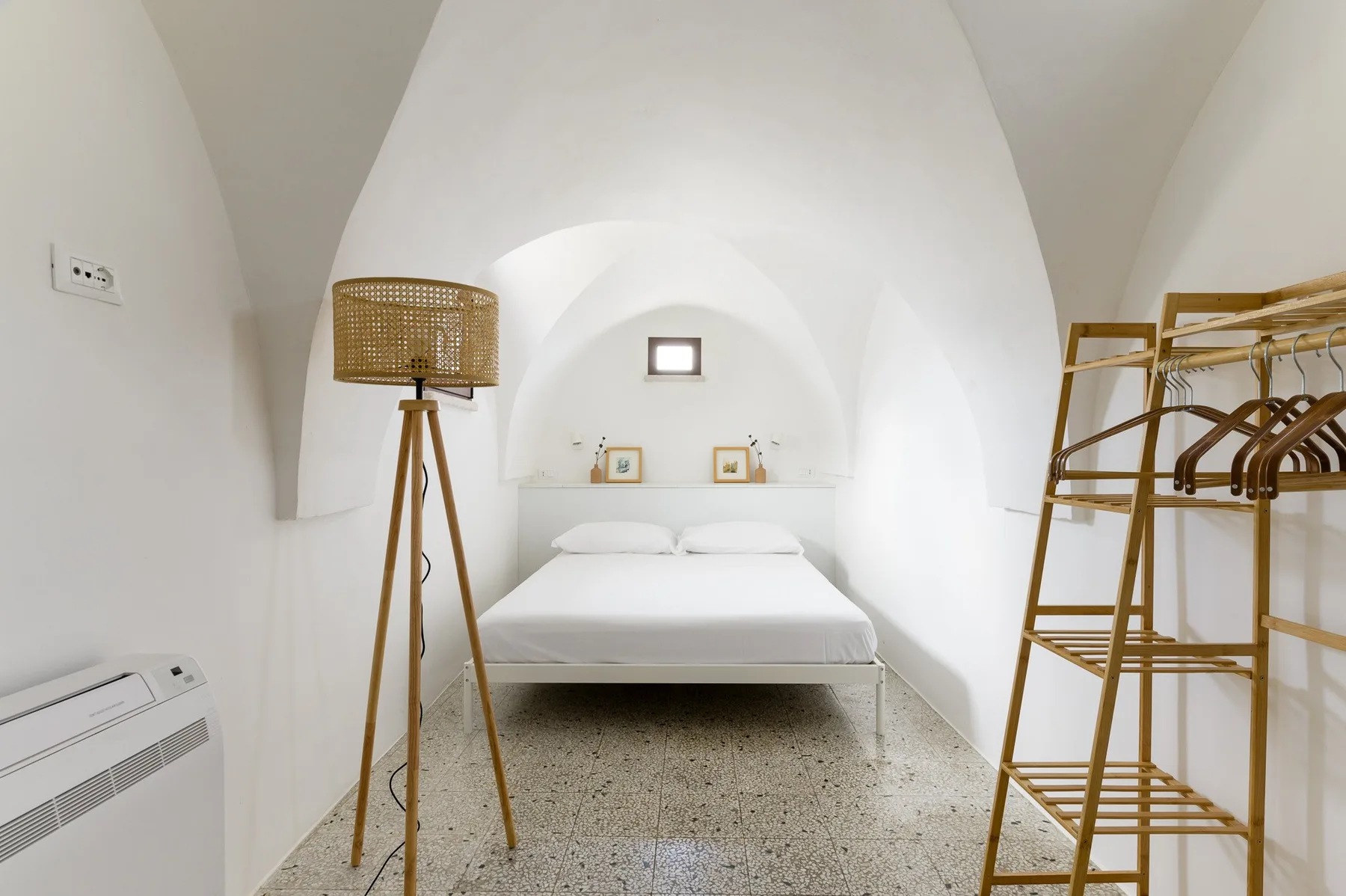 A bedroom with a bed, a floor lamp, and an open clothing rack.