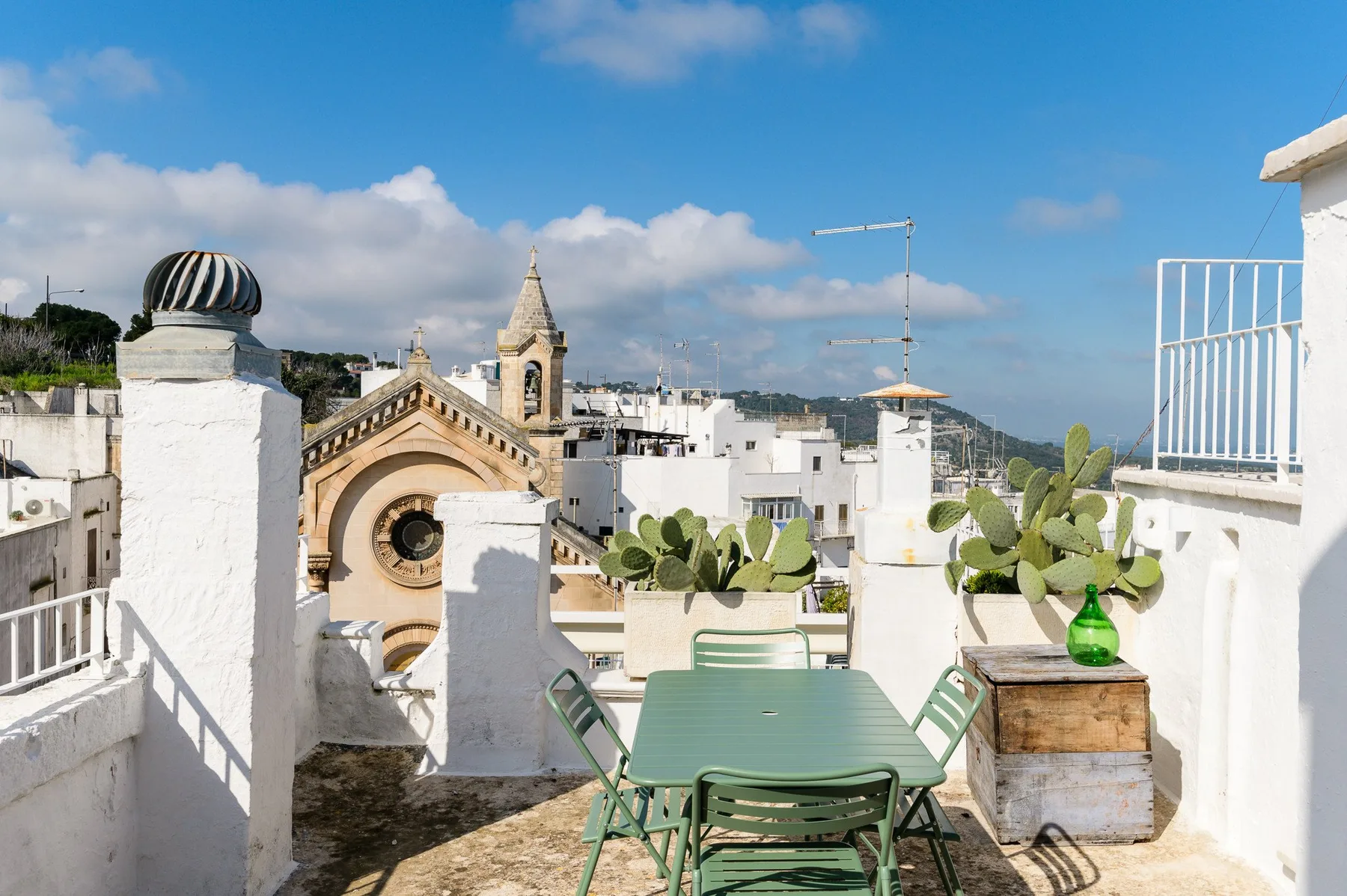 A rooftop terrace with green seating and potted plants overlooks nearby rooftops.