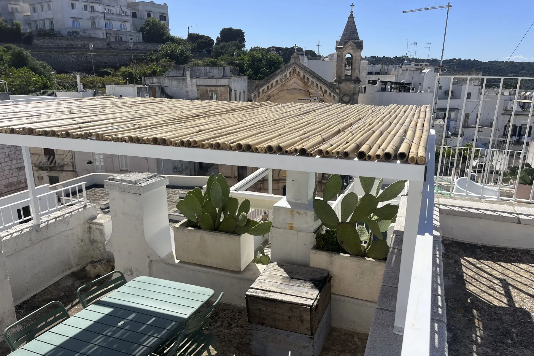 A rooftop terrace has a shaded seating area and potted cactus plants.