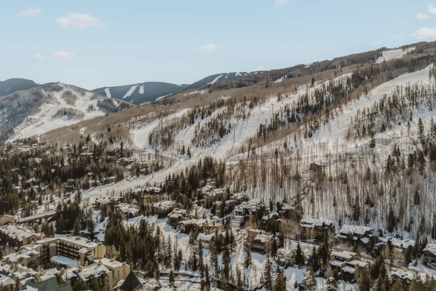 Un complejo de montaña nevado se extiende por laderas boscosas bajo un cielo despejado.