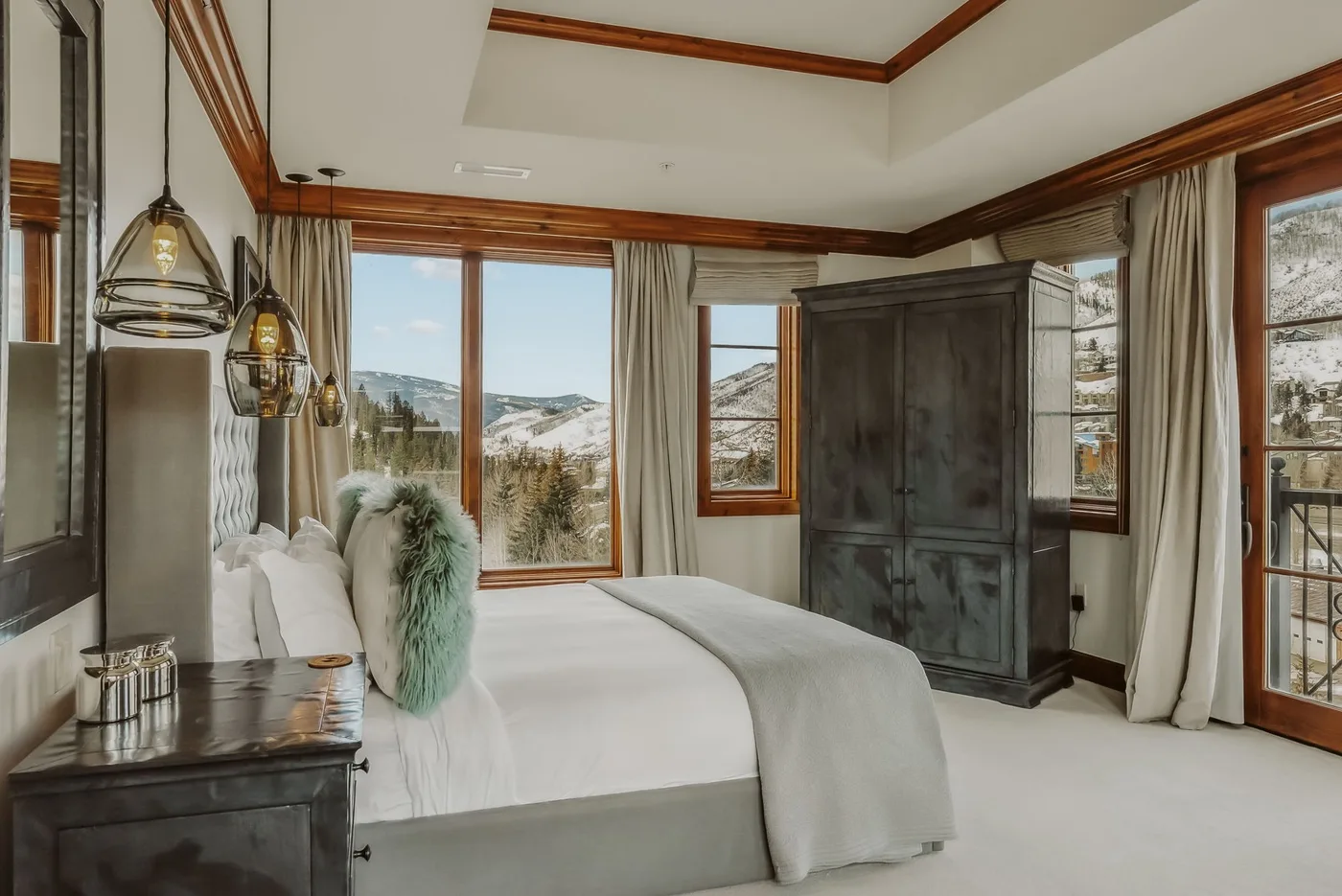 Un dormitorio luminoso con una cama grande, ventanas con cortinas y un armario oscuro.