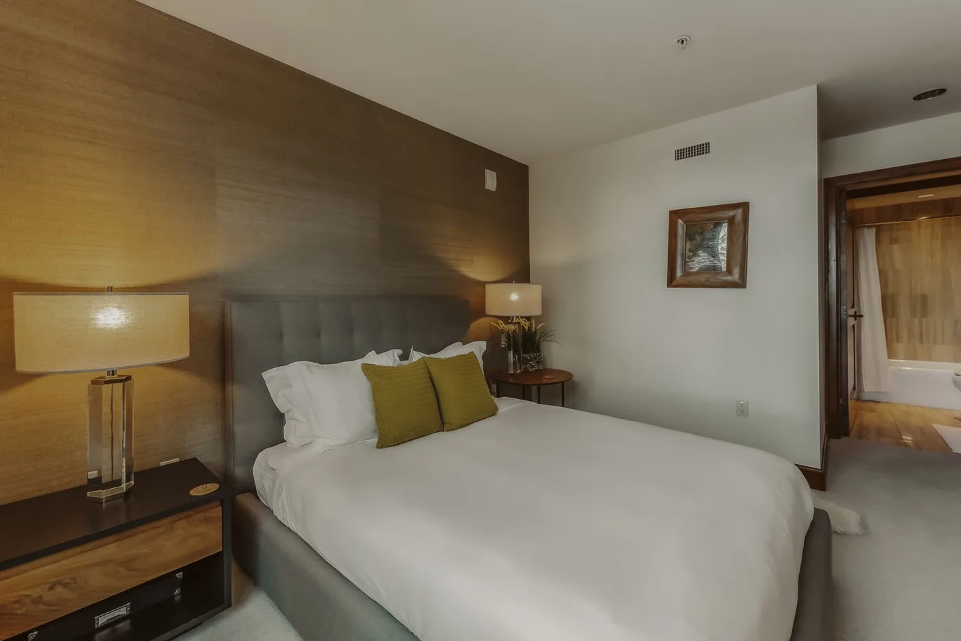 Un dormitorio con una cama tendida, lámparas de noche y un cuadro en la pared.