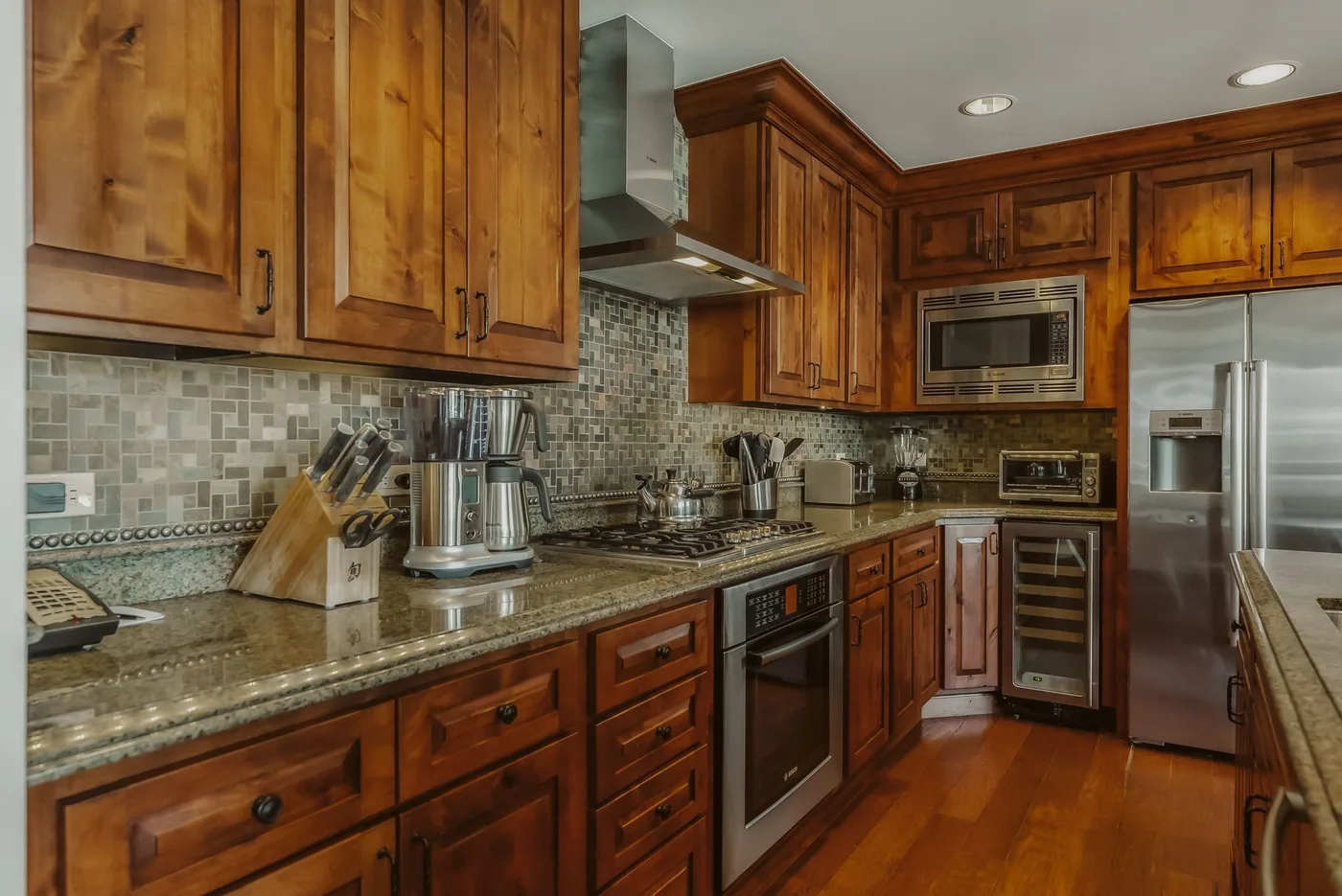 Una cocina con gabinetes de madera, encimeras de granito y electrodomésticos de acero inoxidable.