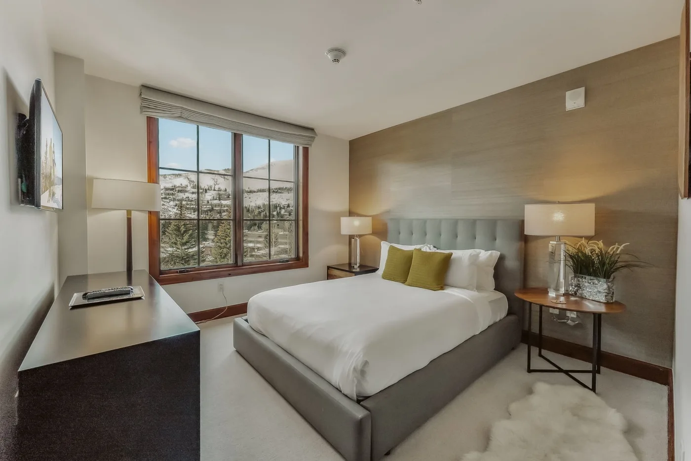 Un dormitorio con una cama bien tendida, mesitas de noche y una ventana grande.