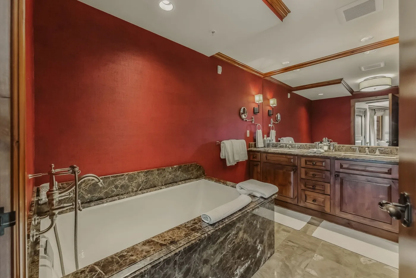 Un baño con una bañera grande, paredes rojas y un tocador de madera.