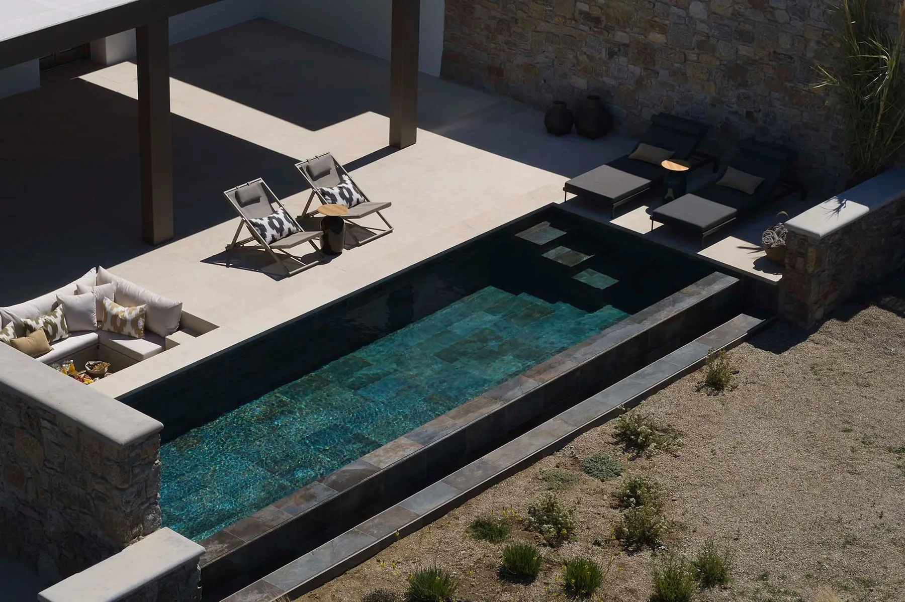 Una piscina rectangular junto a un patio pavimentado con asientos de descanso.
