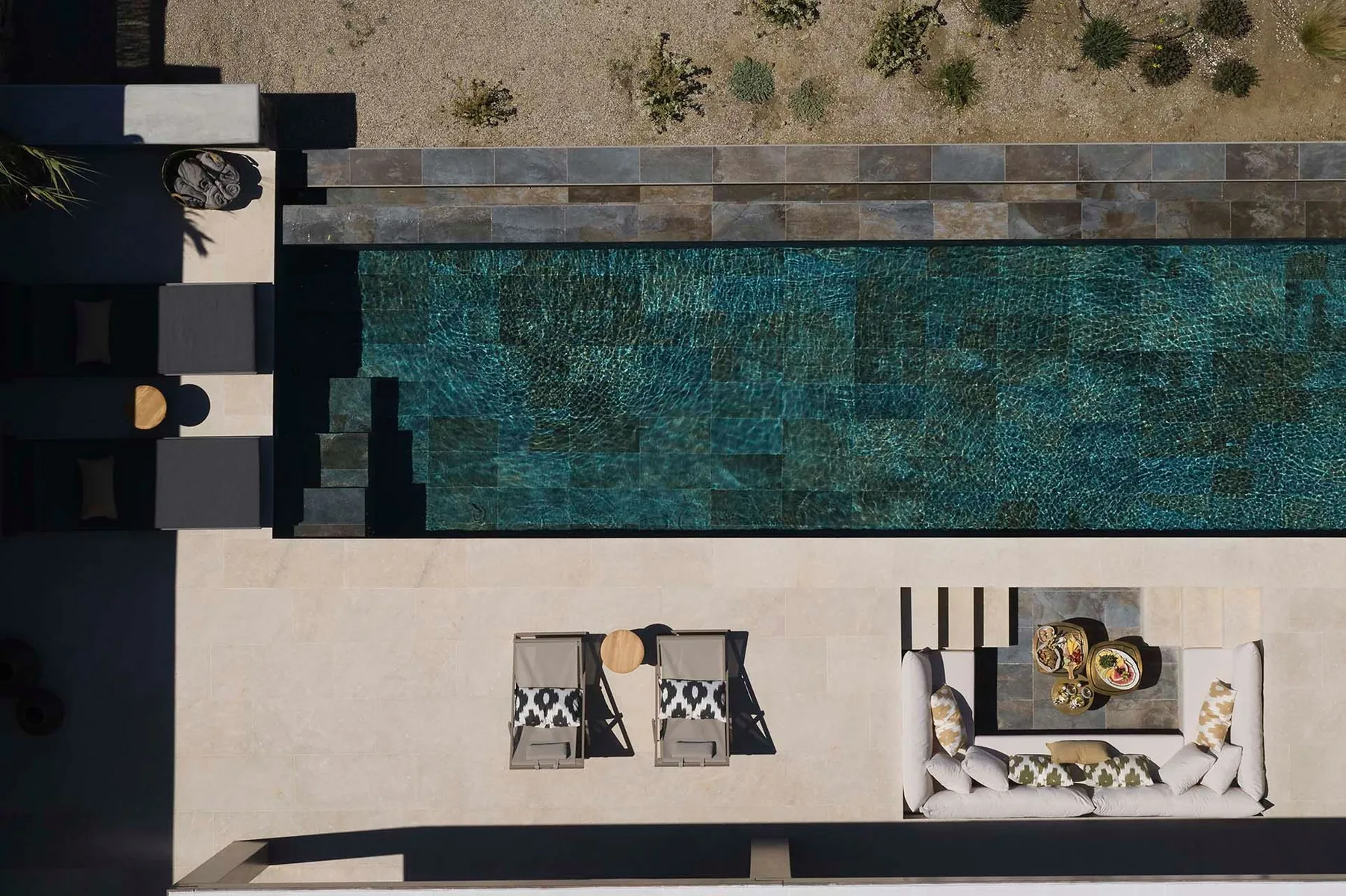 Una piscina exterior junto a una terraza pavimentada con asientos.
