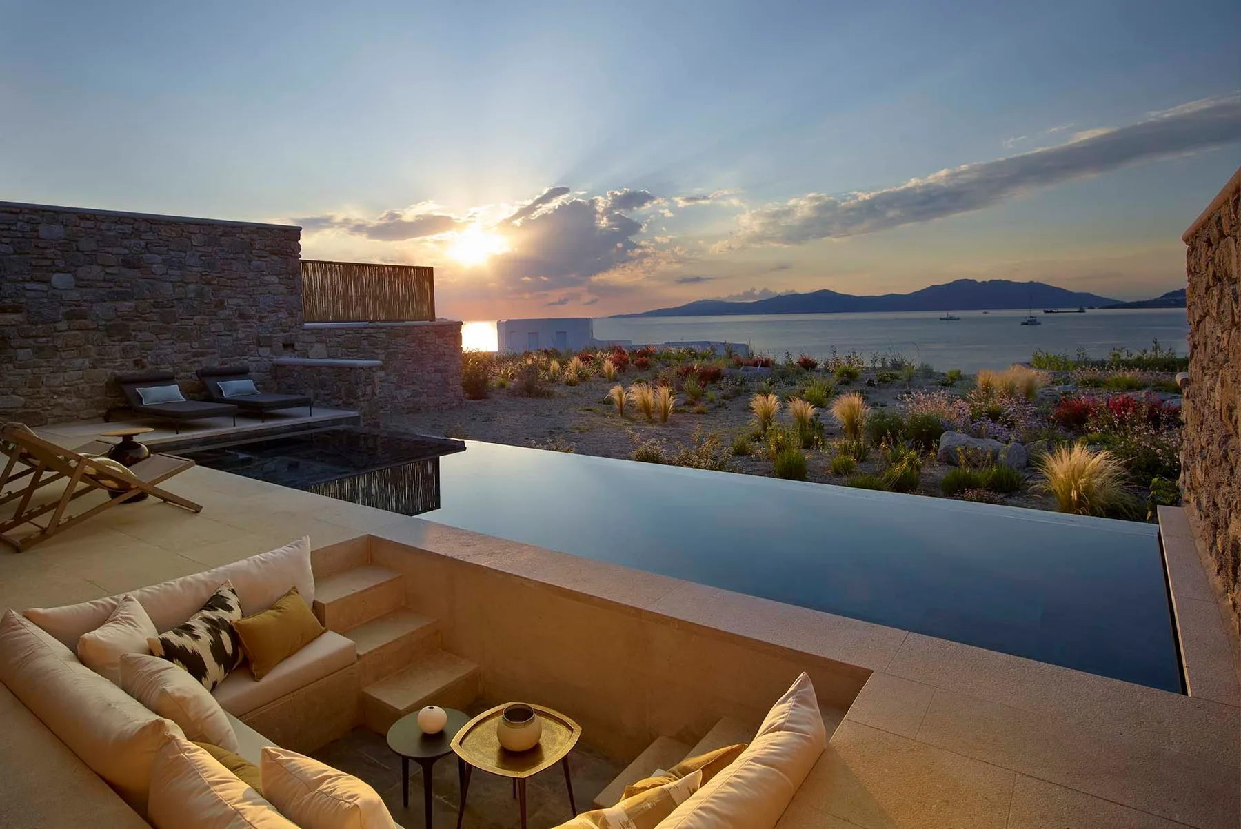 Una zona de descanso al aire libre y una piscina infinita miran al mar al atardecer.