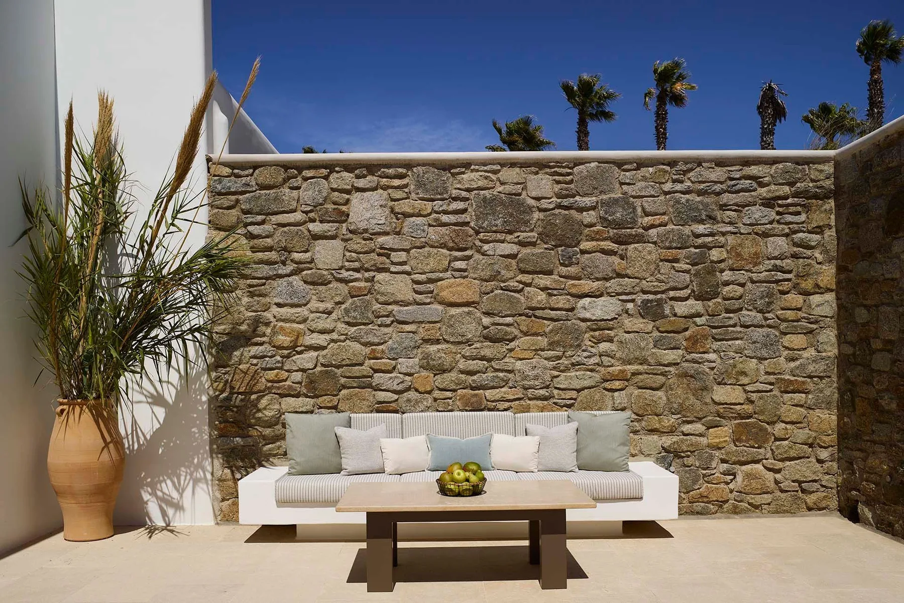 Una zona de estar en un patio con una mesa baja frente a un muro de piedra.