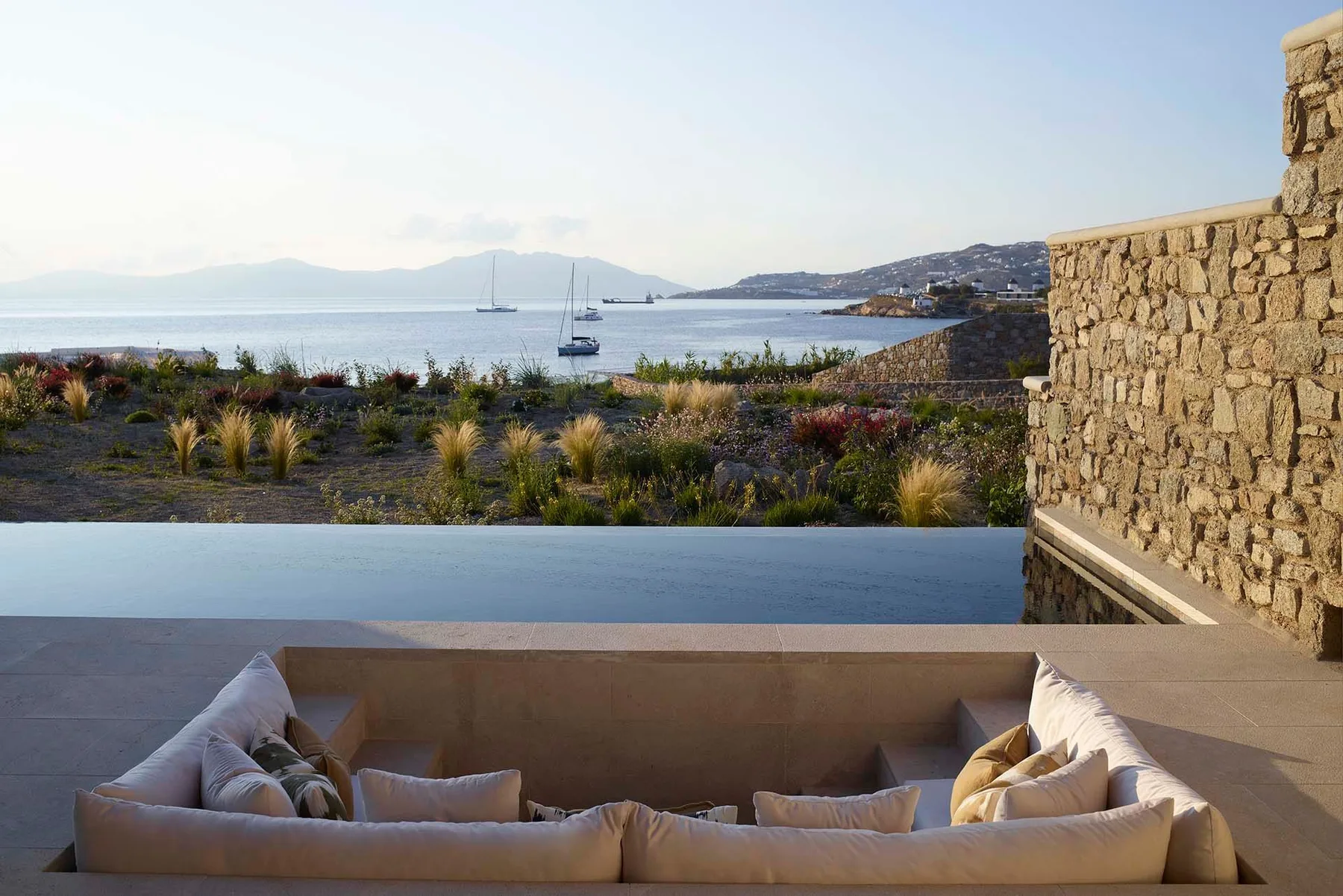 Una terraza junto al mar con asientos acolchados da al agua y a veleros.