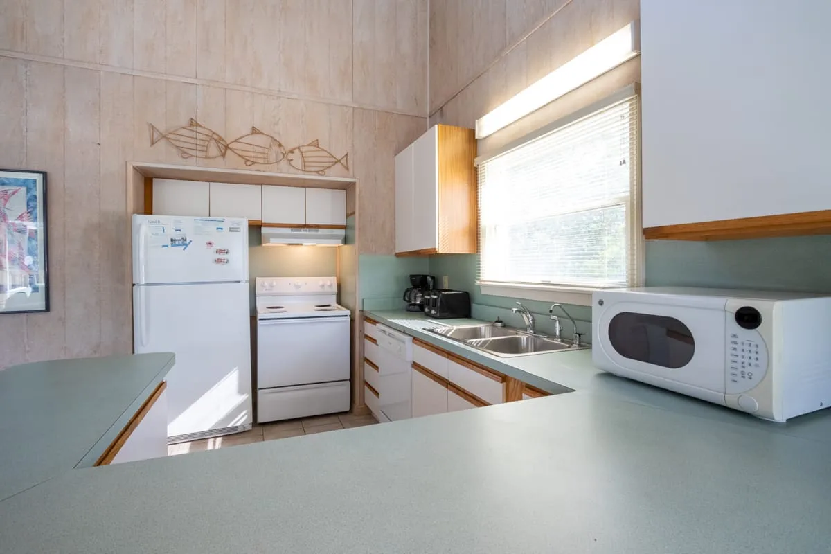Una cocina con encimeras claras, refrigerador, estufa y microondas.