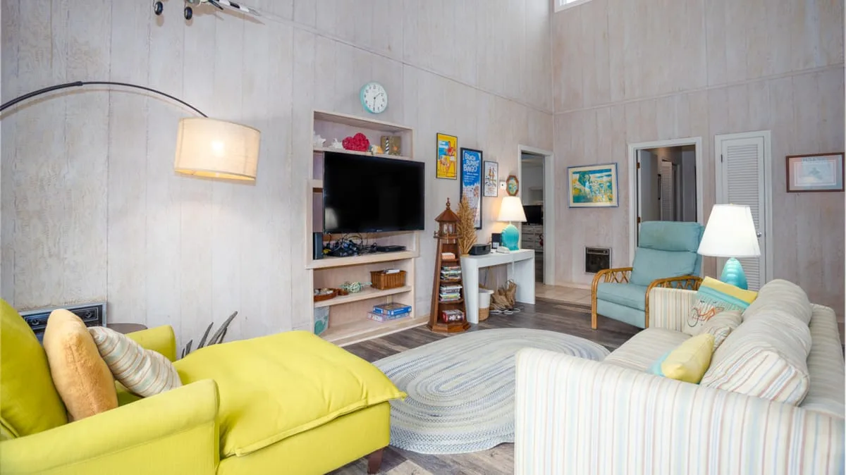Una sala luminosa con asientos coloridos, un televisor y una alfombra estampada.