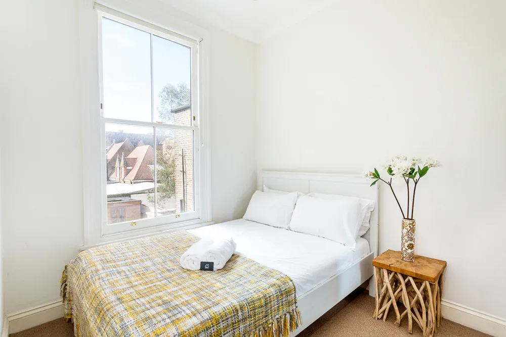 A bright bedroom with a bed beside a large window.