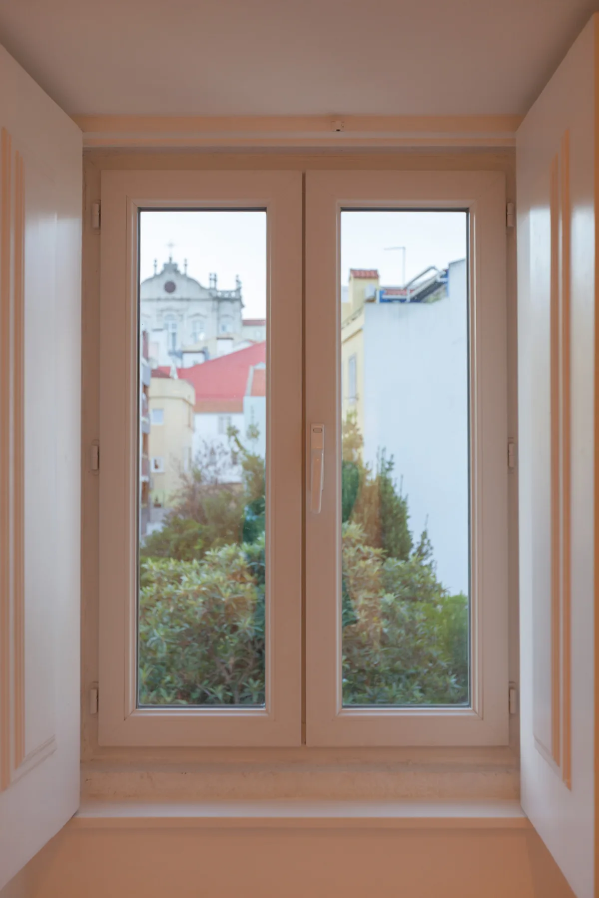 Un rincón luminoso con ventana ofrece vistas a árboles frondosos y edificios vecinos.