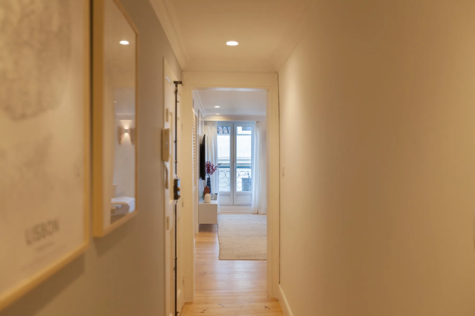 Un pasillo conduce a una habitación luminosa con ventanas y suelo de madera clara.