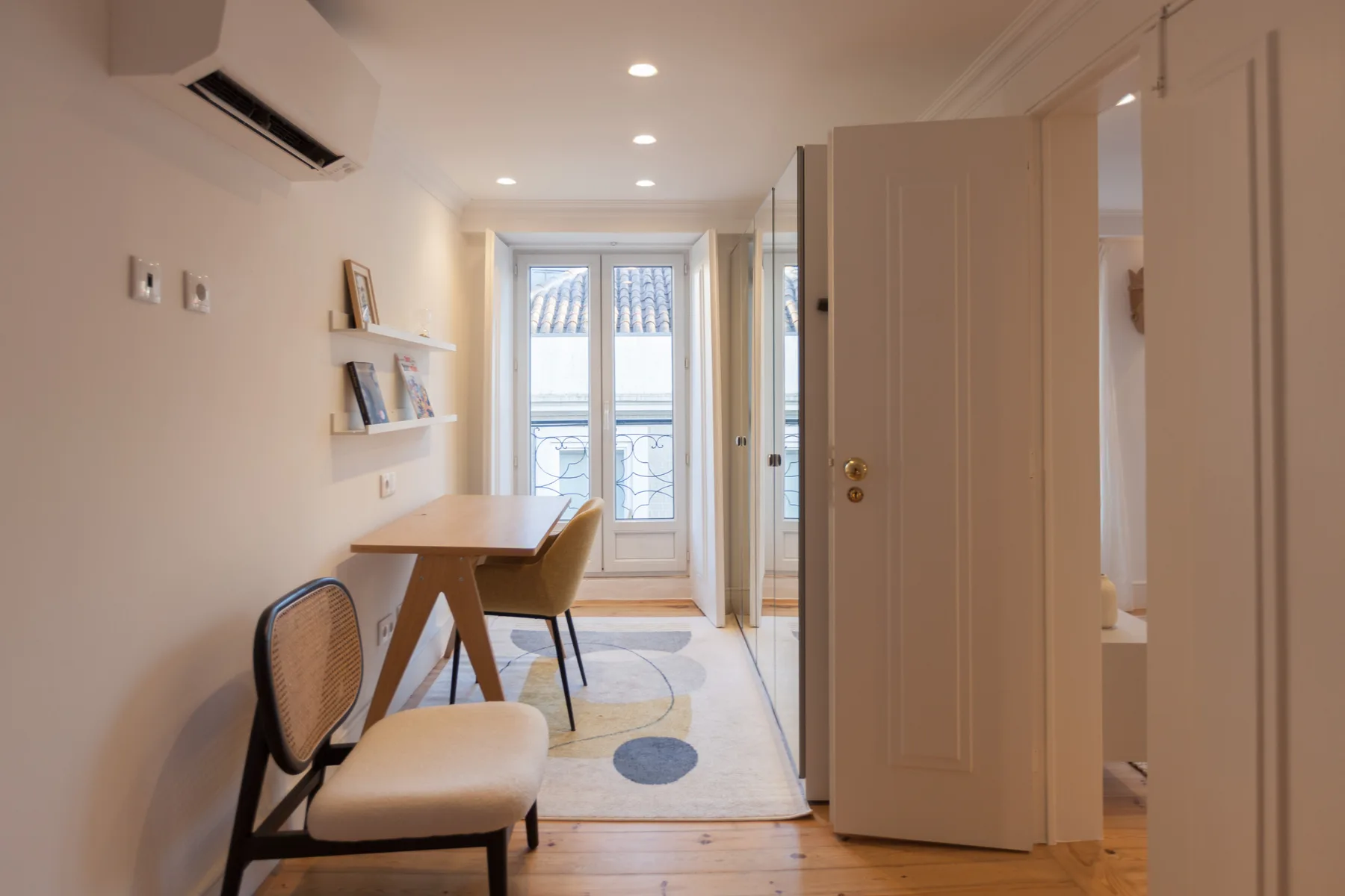 Una habitación luminosa con una mesa pequeña y sillas junto a ventanas altas.