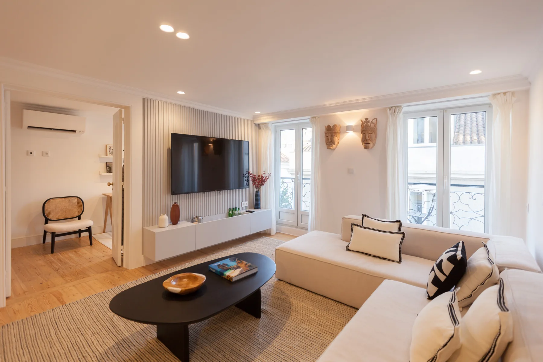 Sala de estar con asientos, un televisor y ventanales.