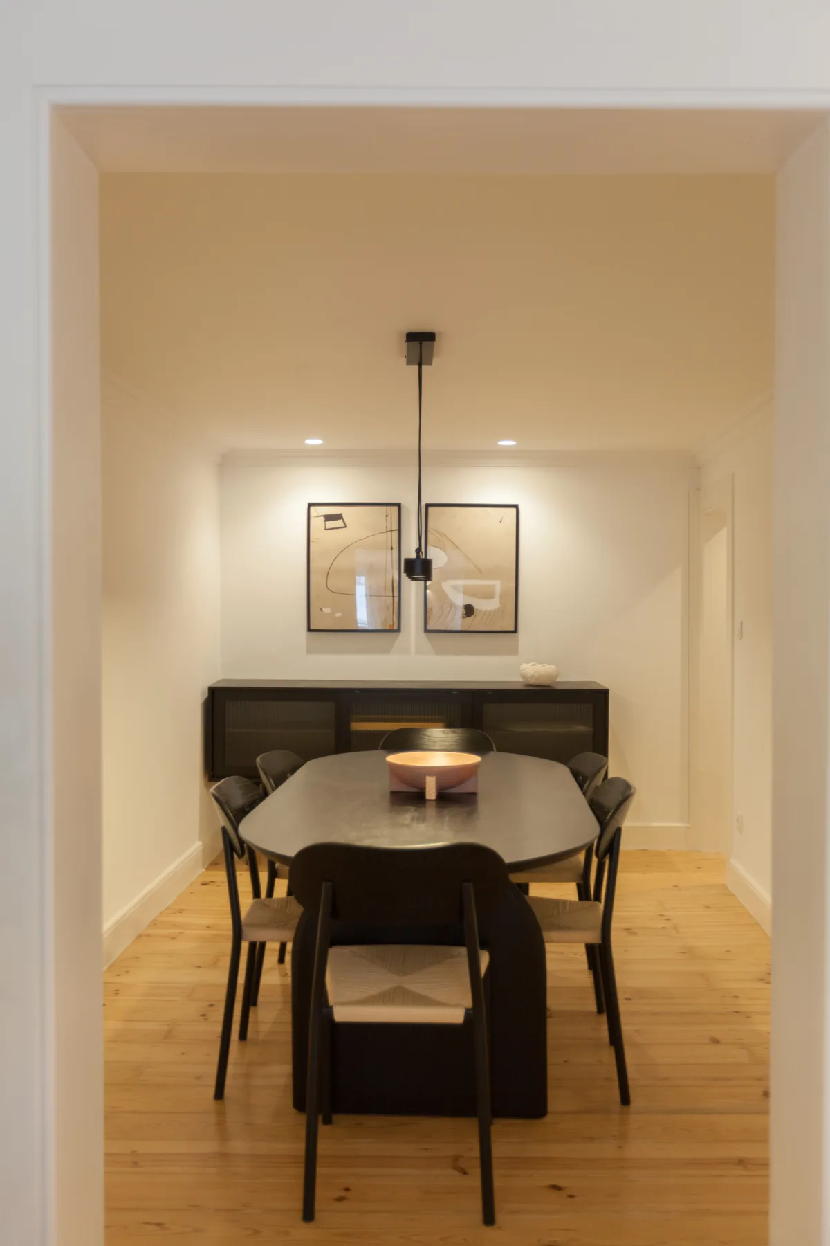 Comedor con una mesa, asientos oscuros y cuadros enmarcados.