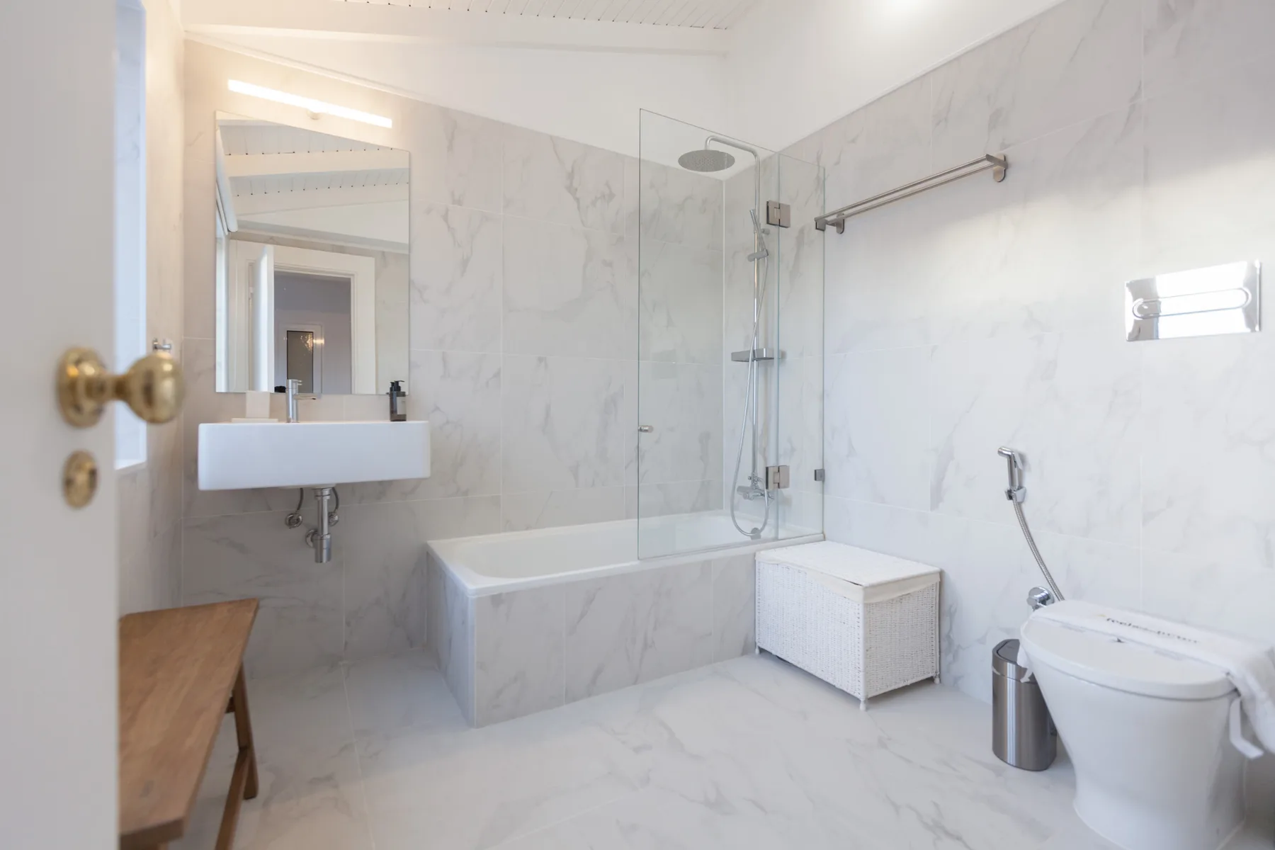Un baño luminoso con bañera, mampara de ducha de vidrio y lavabo suspendido.