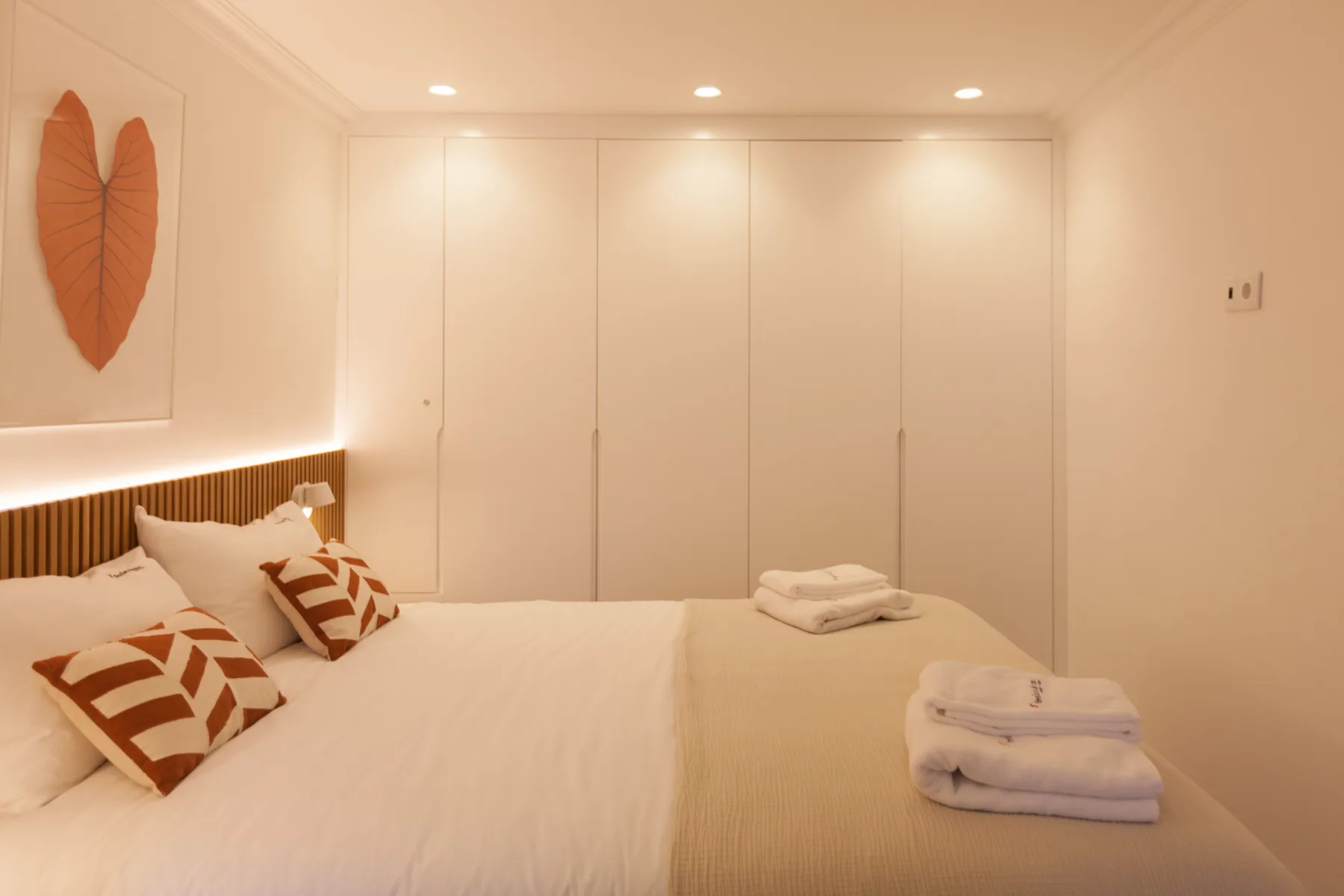 Un dormitorio ordenado con cojines estampados y toallas dobladas sobre la cama.