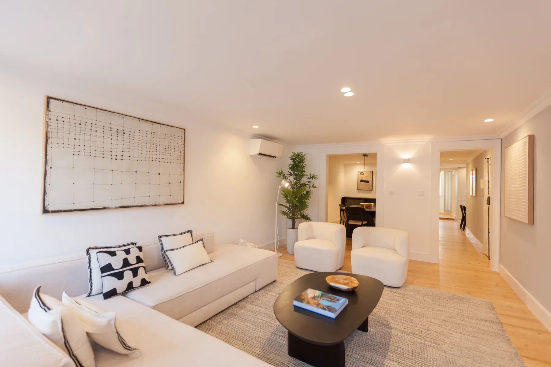 Una sala de estar luminosa con un sofá, sillones y una mesa de centro baja.