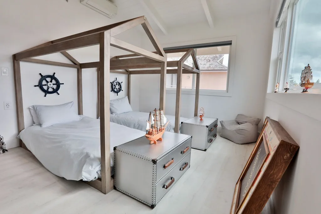 Un dormitorio luminoso con camas con dosel, adornos náuticos y una ventana grande.