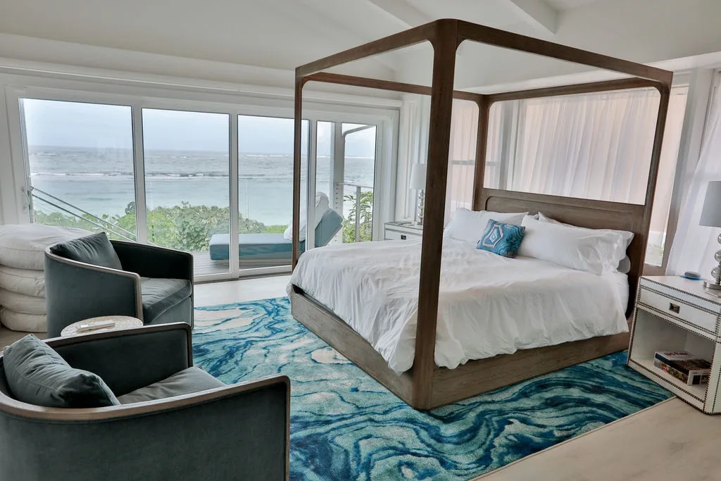 Un dormitorio luminoso con cama con dosel, asientos y amplias ventanas con vistas al agua.