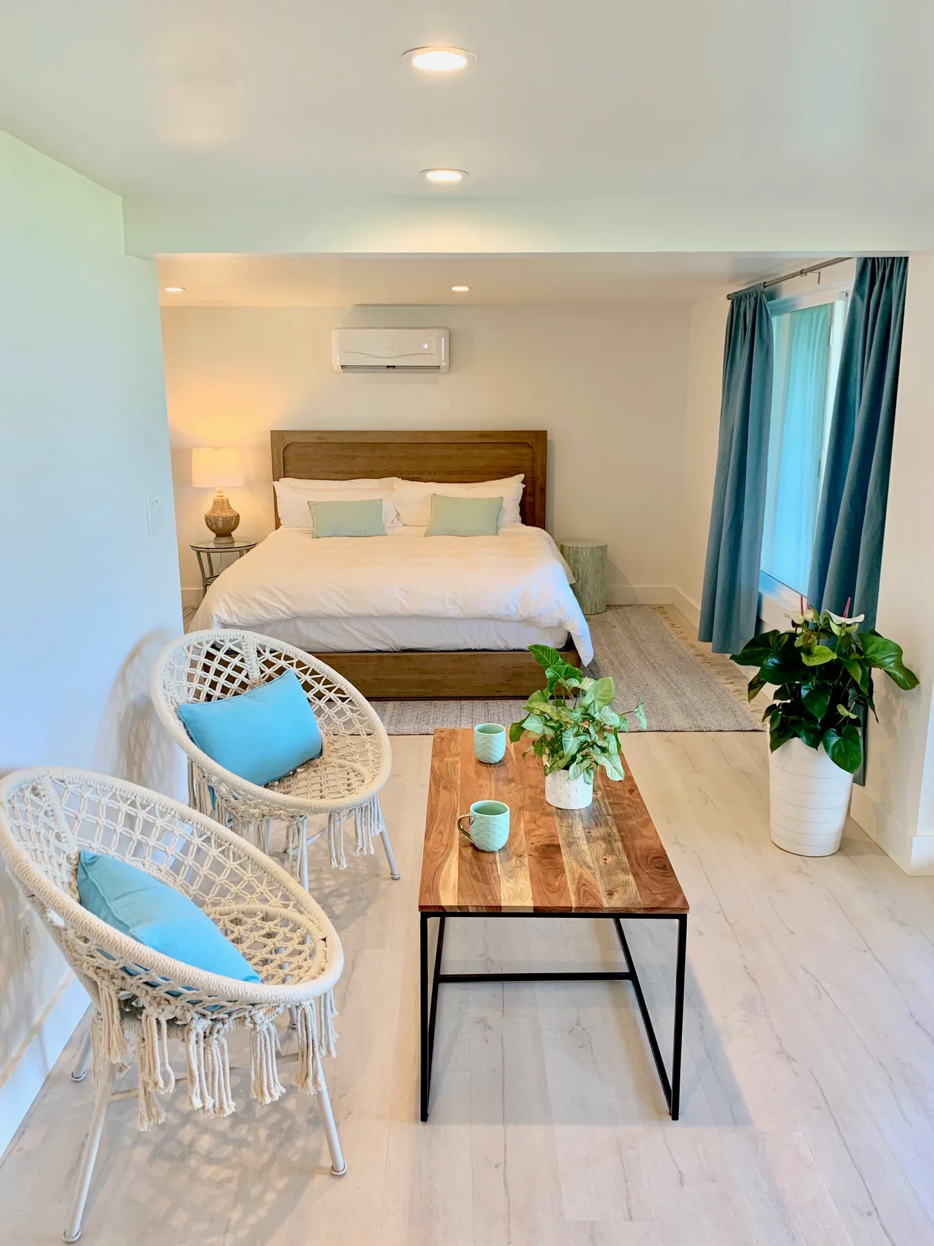 Un dormitorio luminoso con una cama, asientos de mimbre y una mesa de centro de madera.