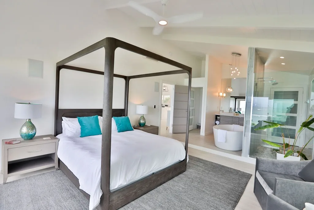 Un dormitorio con una cama con dosel oscuro y un baño contiguo visible tras un vidrio.