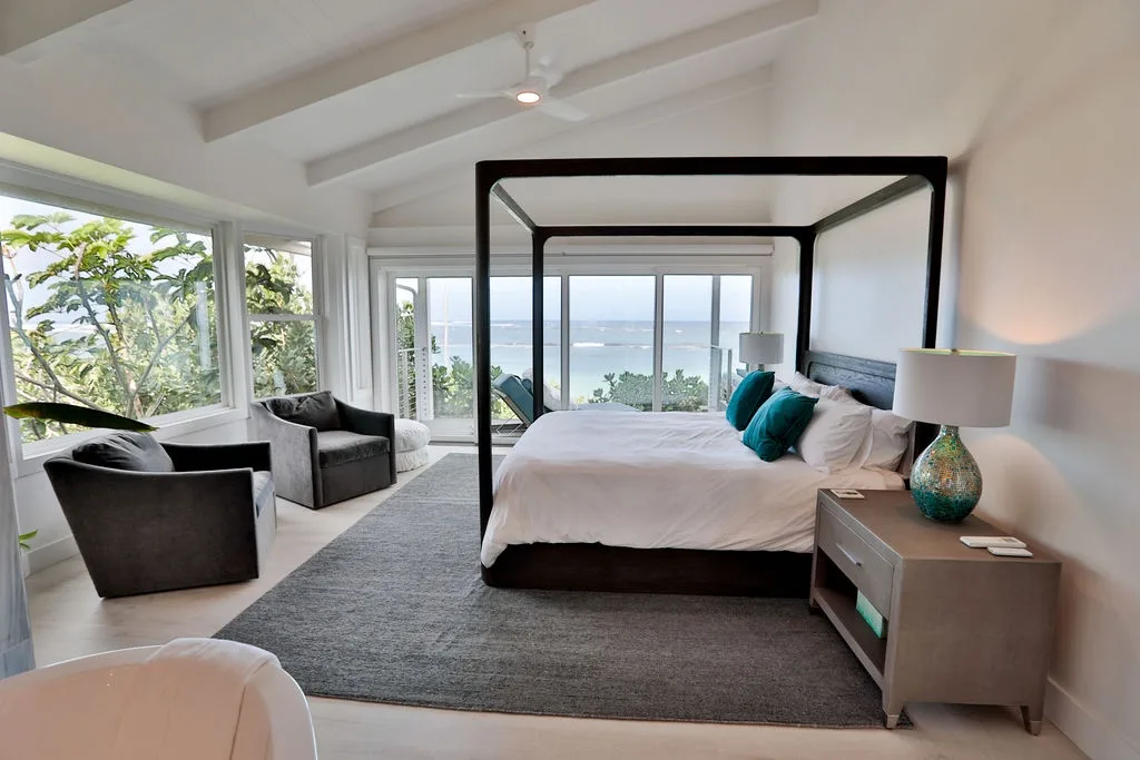 Un dormitorio luminoso con cama con dosel, asientos y grandes ventanas con vistas al agua.