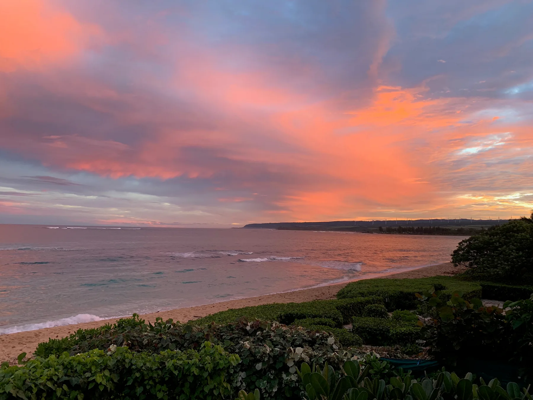 Una playa costera al atardecer bajo un cielo lleno de nubes coloridas.