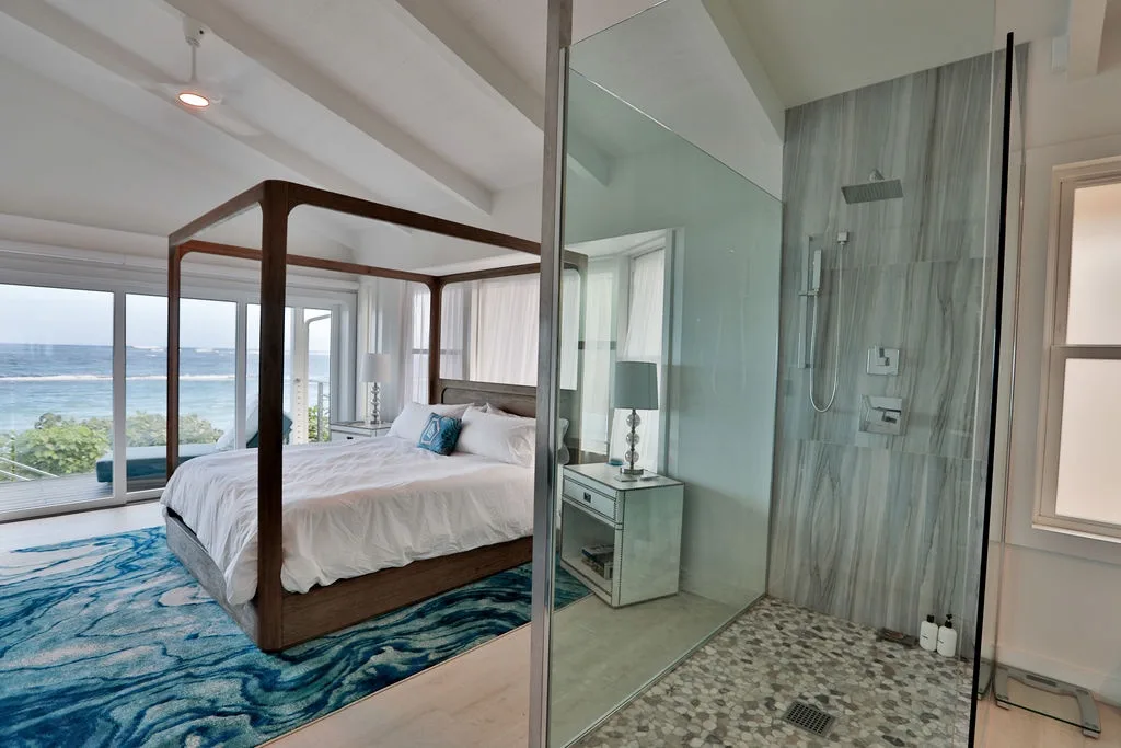Un dormitorio con cama con dosel junto a una ducha de vidrio y grandes ventanas.