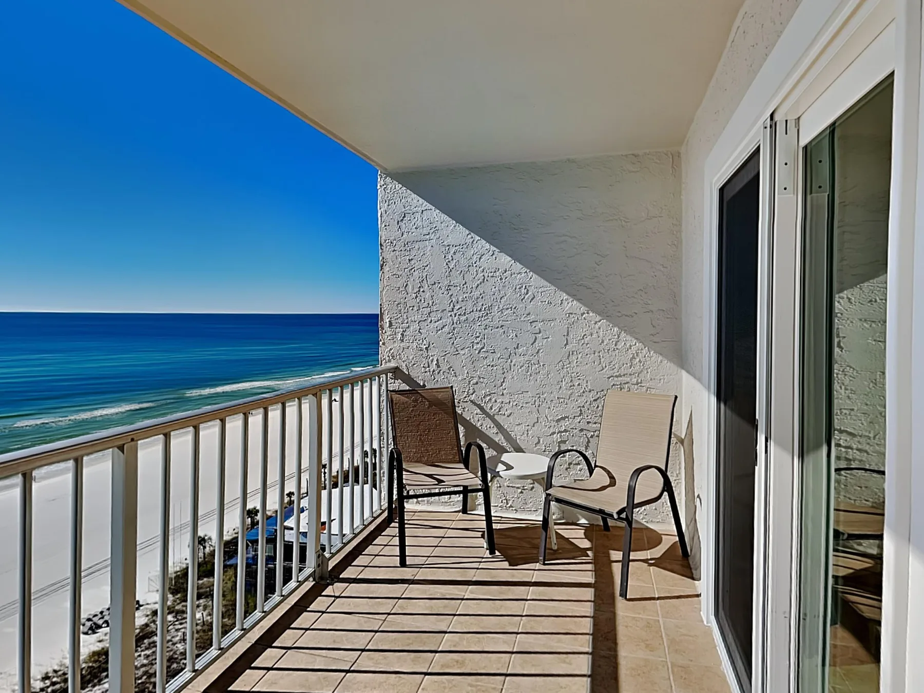 A seaside balcony with seating overlooks the ocean and beach.