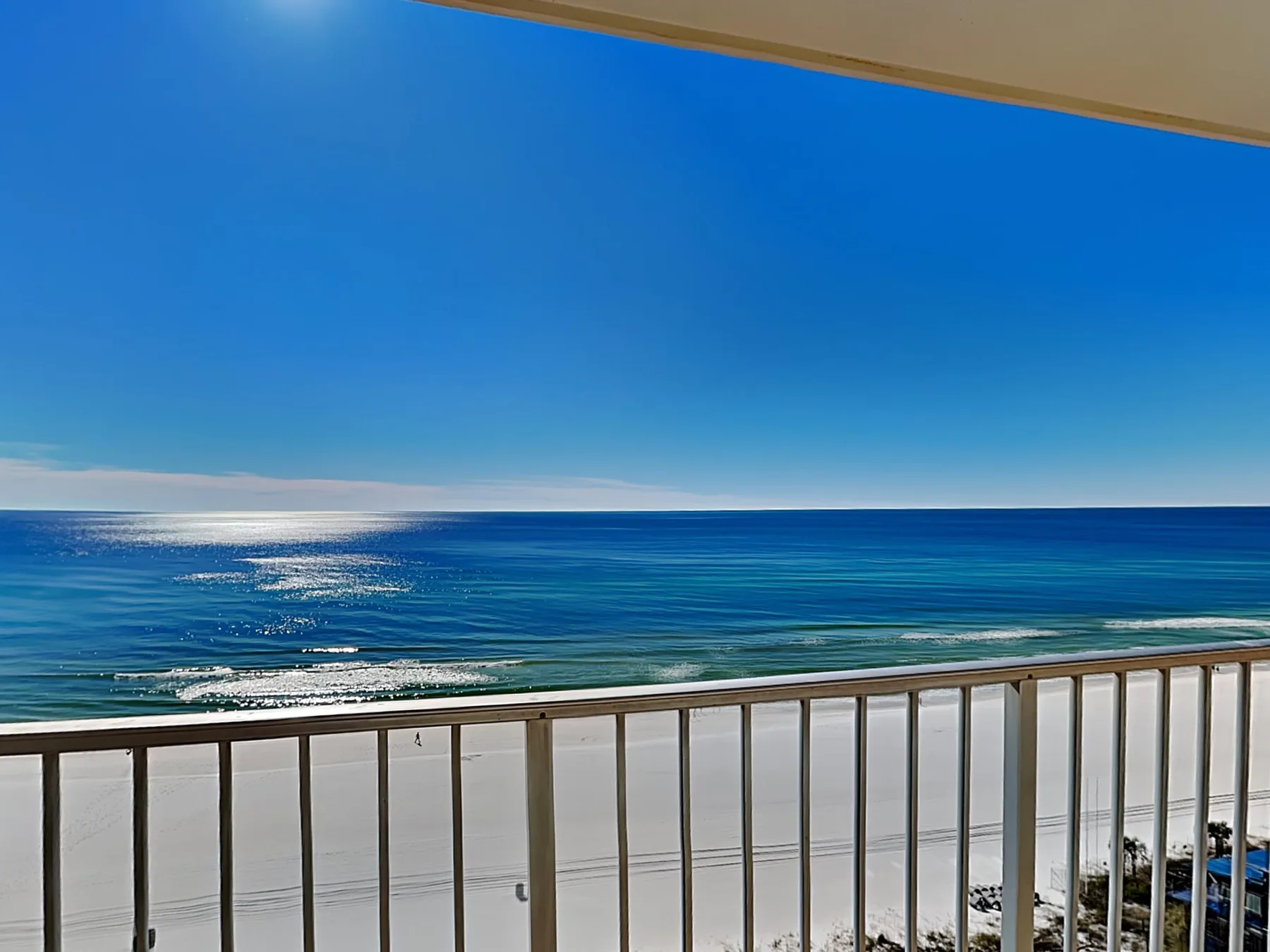 A balcony overlooks the ocean and a sandy beach beneath a clear blue sky.