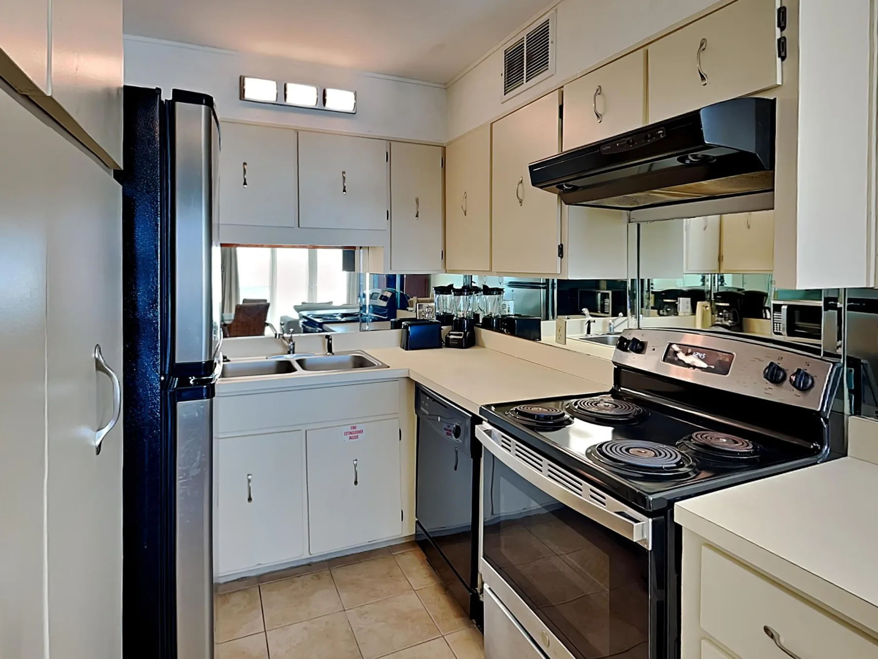 A compact kitchen with white cabinetry, a dark refrigerator, and an electric range.