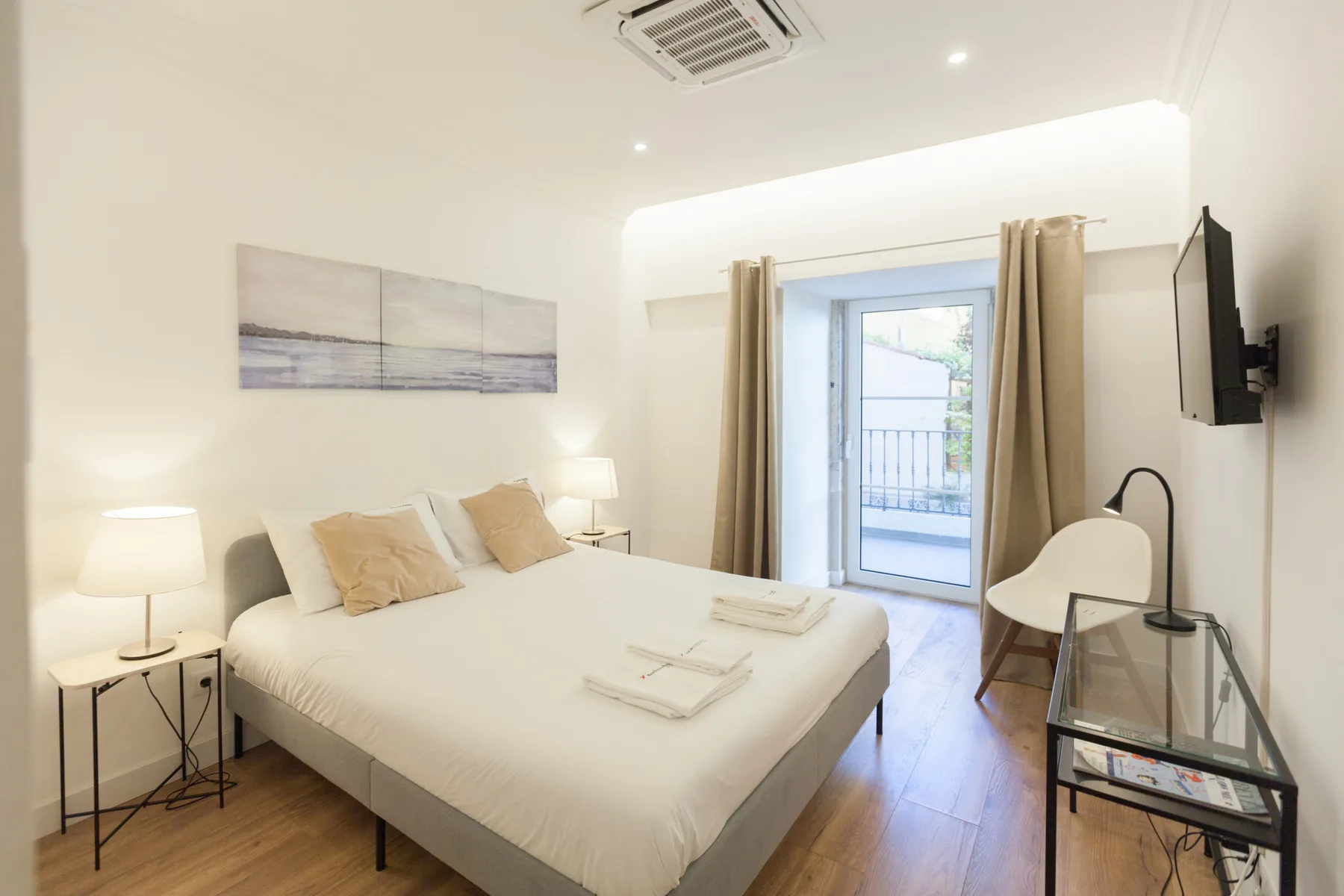 Un dormitorio luminoso con una cama bien arreglada y una puerta de cristal que da a un balcón.