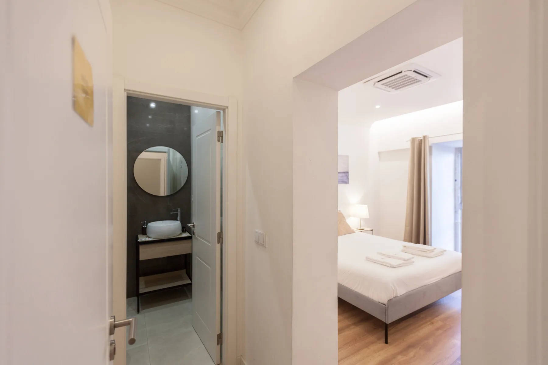 A bedroom with a neatly made bed is visible through an open doorway.
