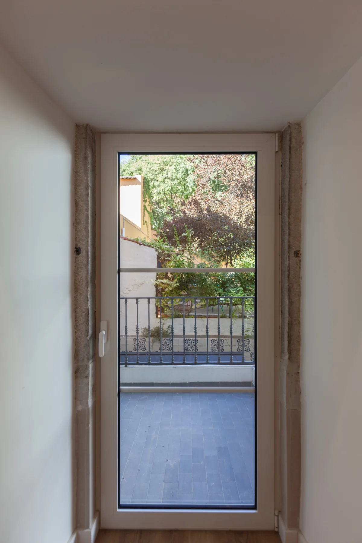 A bright interior doorway opens onto a balcony with greenery beyond.