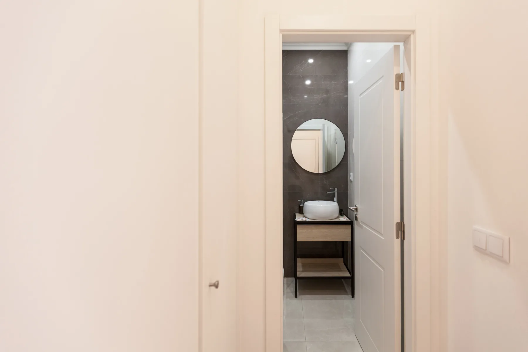 A bathroom vanity and round mirror are visible through an open doorway.
