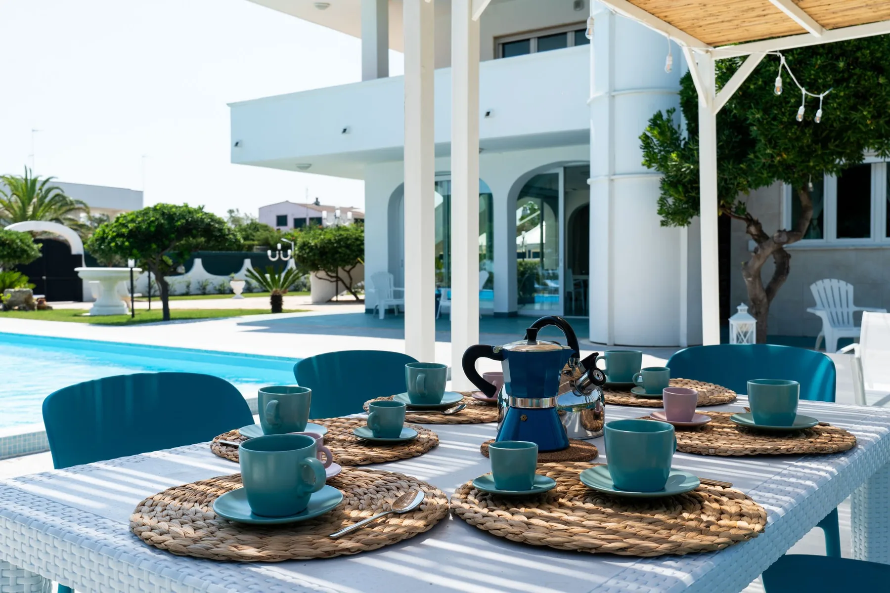 Una mesa junto a la piscina está preparada con tazas y una cafetera.